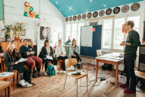 In einem farbig dekorierten und bemahlten Raum sitzen Workshopteilnehmende während Marcus Casutt stehend einen Input gibt